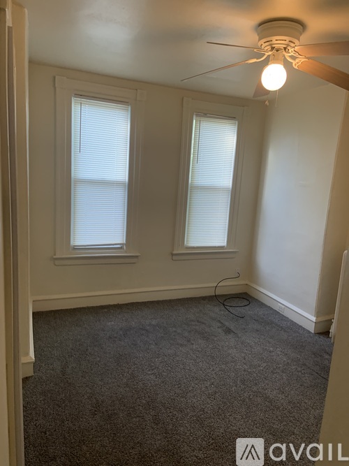 A room with a carpeted floor, a ceiling fan, and two windows.