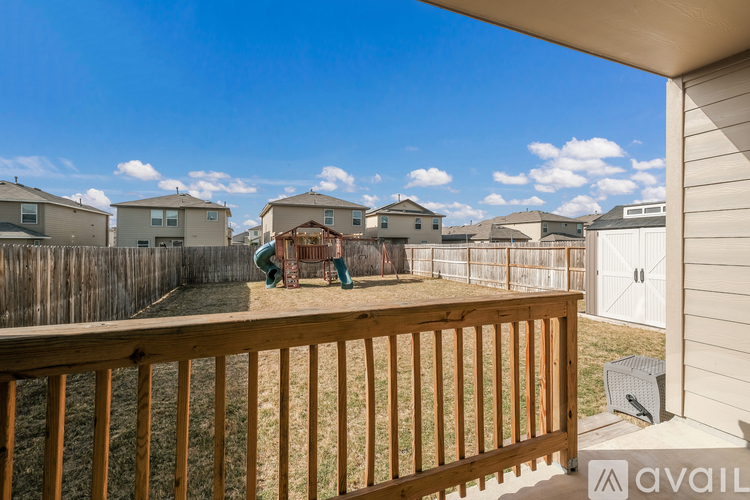 A wooden deck with a railing overlooks a grassy area with houses in the background.