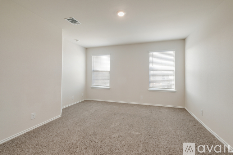 A spacious room with carpeted floor and two windows with blinds.