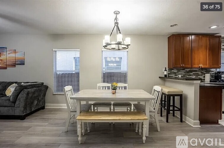 A dining room with a white table and chairs, a couch, and a kitchen area in the background.
