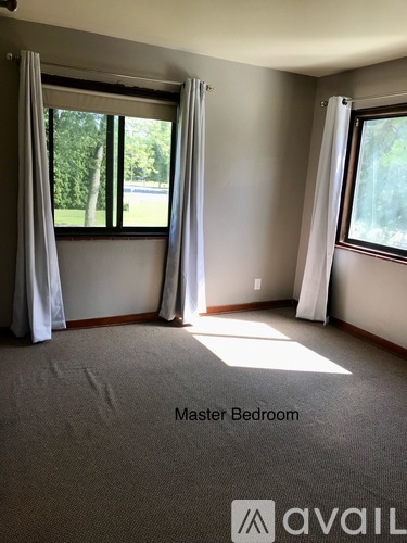 A master bedroom with carpeted floor and two windows.
