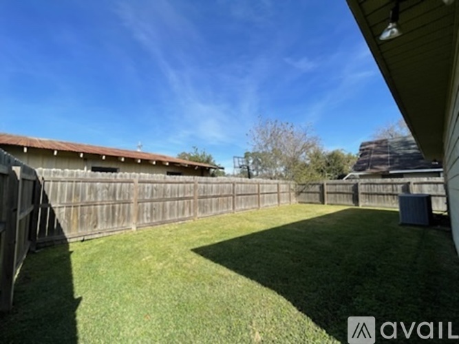 A backyard with a wooden fence and a blue trash bin.