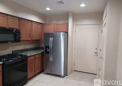 A kitchen with a black stove top oven, a black microwave, a silver refrigerator, and wooden cabinets.