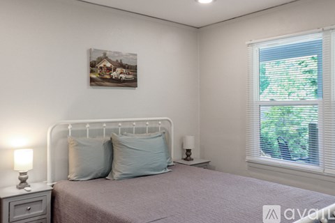 A bedroom with a bed, two pillows, a nightstand with a lamp, and a painting on the wall.