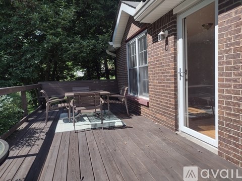 A wooden deck with a table and chairs is in front of a brick house.