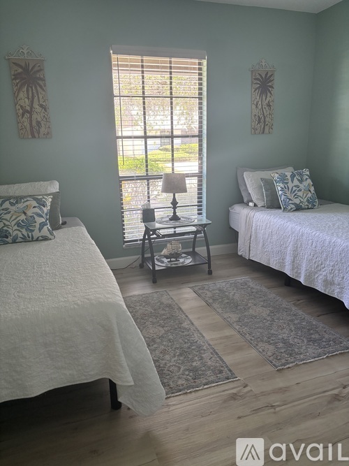 A bedroom with two beds and a window with blinds.