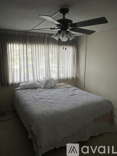 A bedroom with a bed, a ceiling fan, and a window with curtains.
