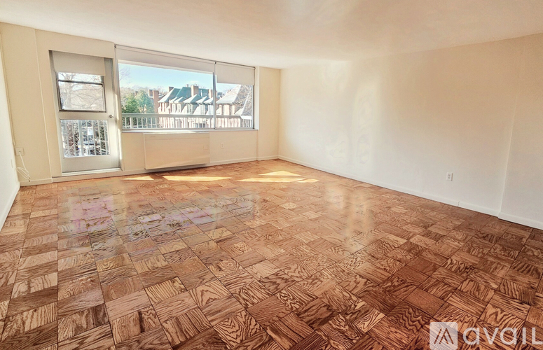 A room with wooden flooring and a view of a street through the window.