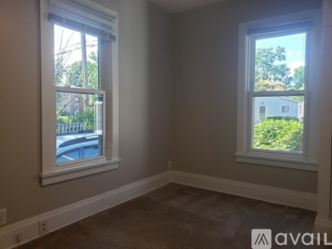 A room with two windows, one showing a street view and the other showing a house and trees.