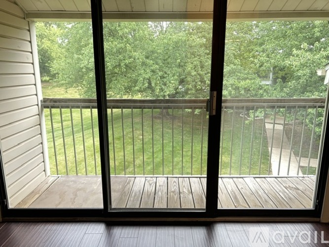 A balcony with a view of a green lawn and trees.