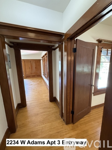 A hallway with wood floors and white walls leading to a door.