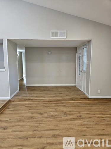 A room with wooden flooring and white walls, with a door on the right side.