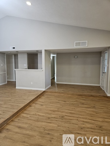 A room with wooden flooring and white walls, with a door on the right side.
