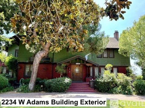 A green house with a red door and a tree in front.