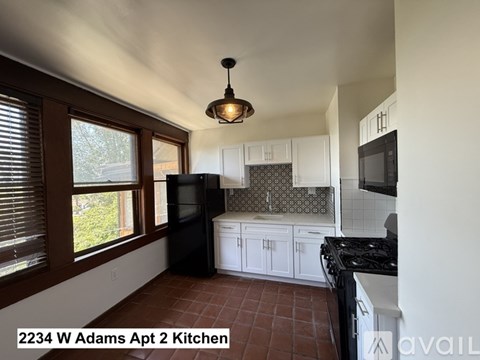 A kitchen with white cabinets and a black fridge is available for rent.