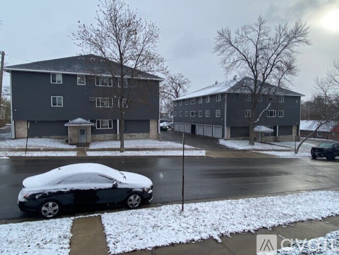 A car is parked on a snowy street in front of a grey building.