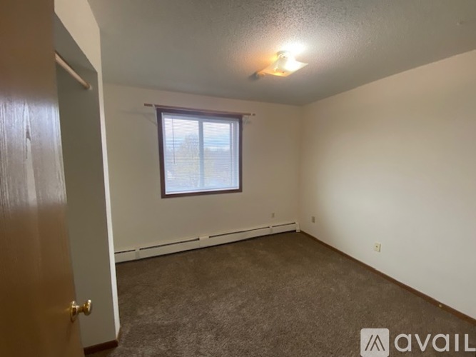 A room with a carpeted floor, a window with blinds, and a door leading to another room.
