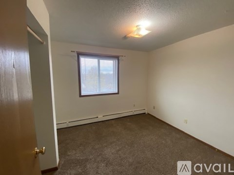 A room with a carpeted floor, a window with blinds, and a door leading to another room.