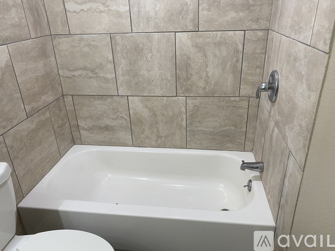 A white bathtub is in a bathroom with a tiled wall.