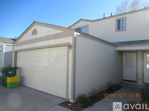 A house with a white garage door and a green recycling bin in front of it.