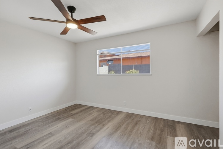 A room with a ceiling fan and a window showing a building outside.