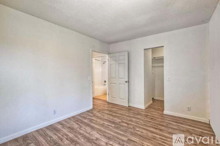 A room with wood flooring and white walls, with a door visible in the background.