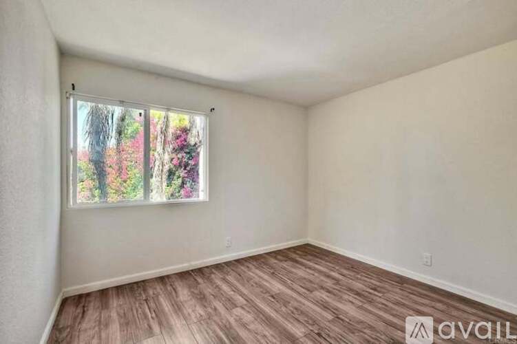 A room with a window showing a view of trees and flowers.