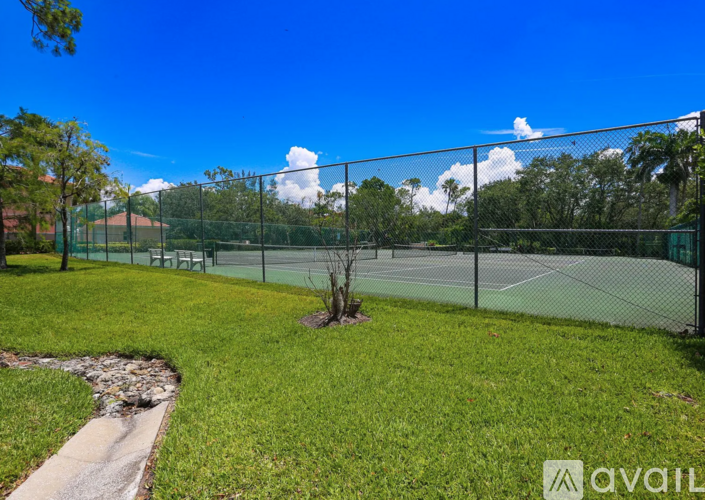 A tennis court surrounded by a green fence and trees.