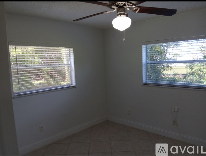 A room with a ceiling fan and two windows with blinds.