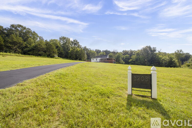 A sign in a grassy field with a house in the background.