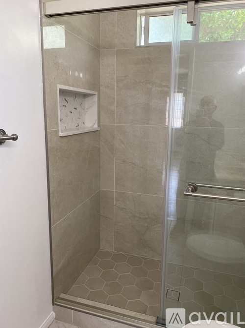 A bathroom with a glass shower door and a tiled floor.