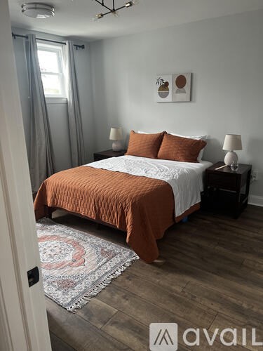 A bedroom with a bed covered in an orange bedspread and two lamps on either side of the bed.