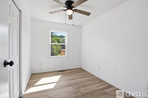 A room with a ceiling fan and a window showing greenery outside.
