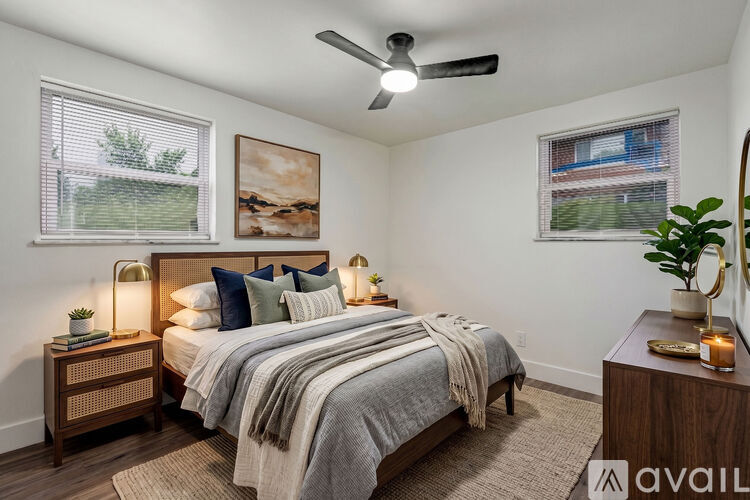 A bedroom with a bed, two lamps, a ceiling fan, and a painting on the wall.
