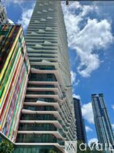 A tall building with a pointed top is in the foreground with a blue sky and clouds in the background.