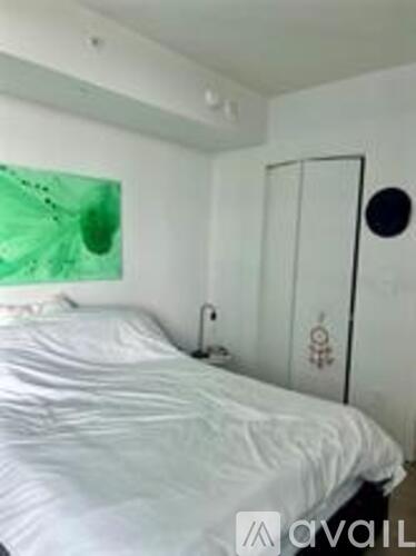 A bedroom with a white bed and a green painting on the wall.