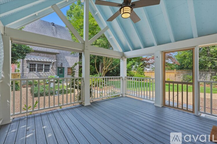 A covered deck with a ceiling fan and a view of a house and trees.