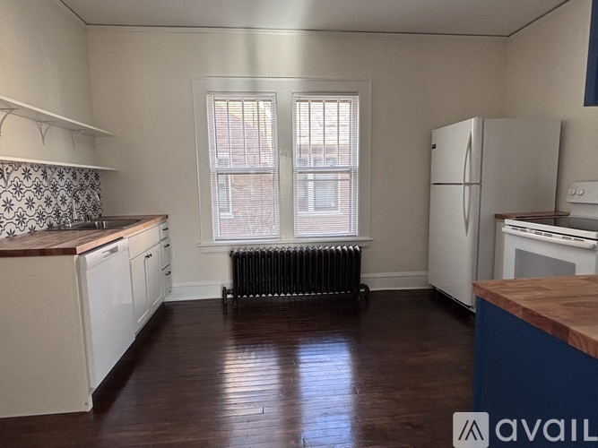 A kitchen with a white refrigerator and a black radiator under a window.