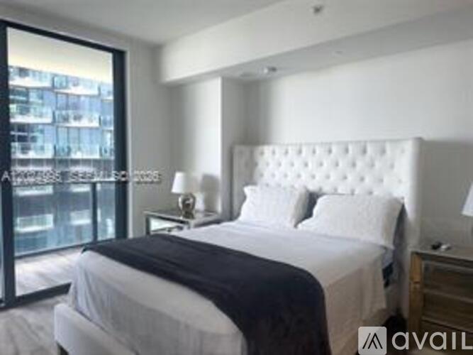 A bedroom with a large bed and a view of a cityscape through a glass door.