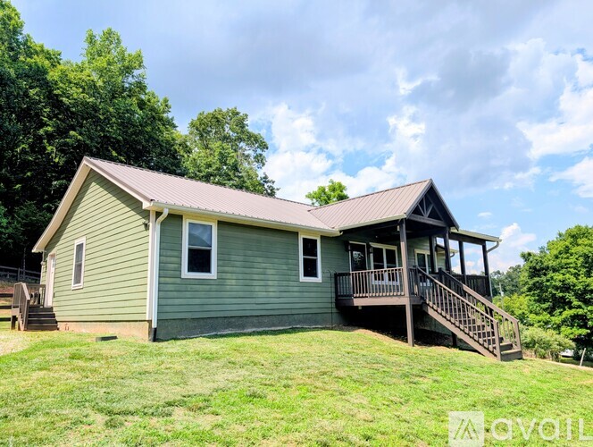 A house with a green siding and a brown roof with a deck and stairs leading to the front door.