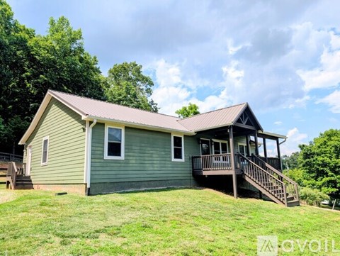 A house with a green siding and a brown roof with a deck and stairs leading to the front door.