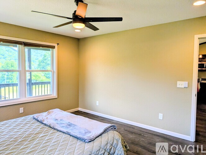 A bedroom with a bed, a ceiling fan, and a window with a view of a deck.