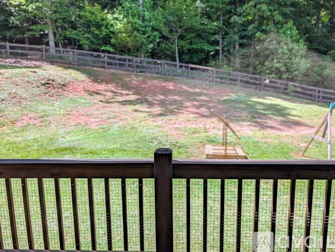 A wooden fence with a green lawn and trees in the background.
