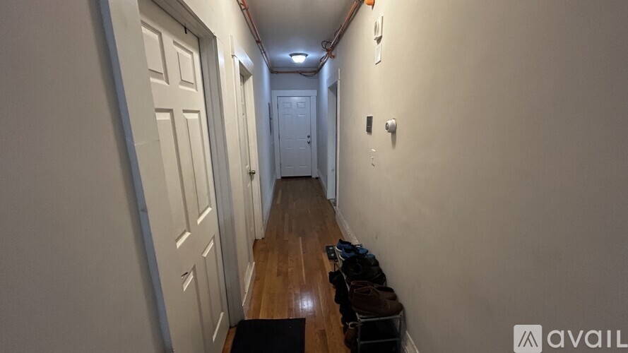 A long hallway with doors on the left and a bench with bags on the right.