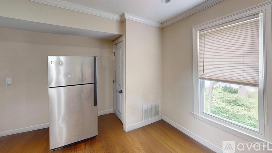 A stainless steel refrigerator in a room with wooden flooring and a window with blinds.