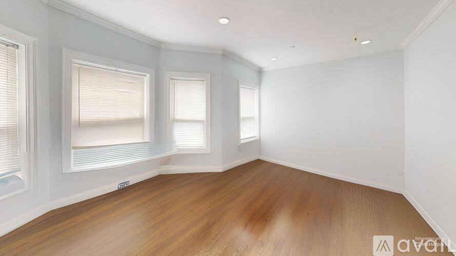 A room with wooden flooring and two windows.