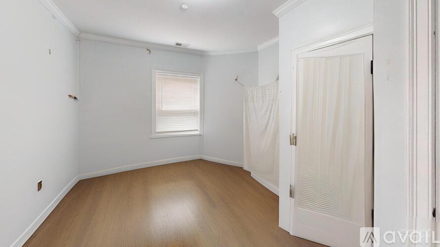 A room with wooden floors and white walls, with a window and a door.
