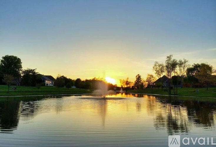 A serene lake with a fountain in the middle surrounded by houses and trees.