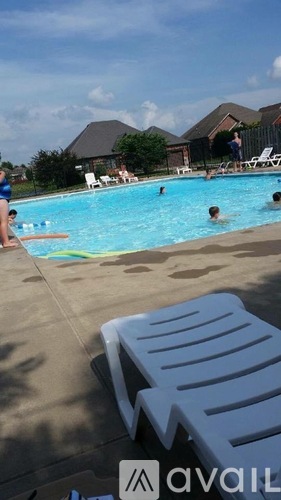 A pool with people swimming and lounging chairs on the side.