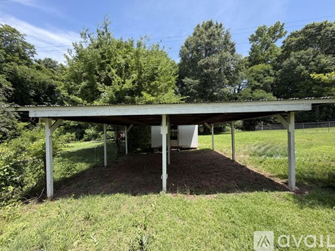 A covered pavilion is situated in a grassy area with trees in the background.